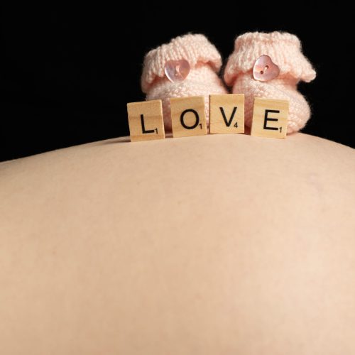 Lettres de scrabbles et chausson de naissances sur un ventre de femme enceinte.